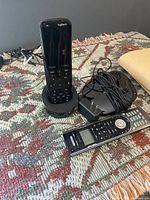 Black Logitech remote standing in charging cradle with hub, power adapter and silver Harmony 550 remote alongside