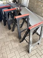 Four black plastic sawhorses with red tops folded and standing