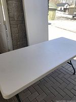 Table unfolded on paved surface showing white plastic top and black folding legs