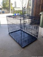 Three-quarter view of black wire dog crate folded open with tray
