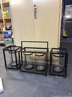 All three black metal hurricane lantern frames with glass inserts displayed