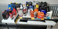 Overall lot on table: multiple jugs, bottles, aerosols, scraper and squeegee