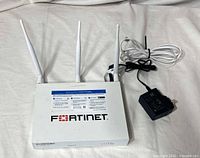 Top view of FortiWiFi 40F with two white antennas attached, power adapter, Ethernet cable and loose black antenna visible