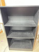 Front view of black 3-shelf bookshelf showing overall structure and wear