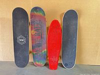 Four complete boards standing upright showing grip sides: Amrgot black, tie-dye, red cruiser, grey grip