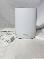 Front view of white Netgear Orbi router with power adapter