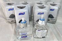 Six white Purell automatic dispensers, five sealed, one unwrapped, and two opened clear refill cartridges