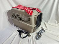 Beige plastic carrier with shirt on top, black and gray jingle-bell straps in front