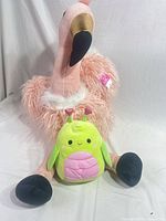 Flamingo plush seated with Squishmallows bug in front