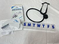 Overview of stethoscope, boxed skin stapler with stapler and remover, and pill organizer