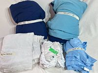 Five bundled bedding items: navy comforter, light blue comforter, polka-dot sheet set, light blue sheet set, white bedskirt