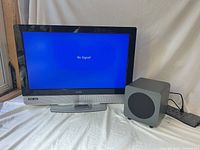Front view of powered-on Vizio TV beside cube subwoofer