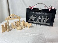 Wooden nativity figures with wooden stable and framed metal nativity wall art displayed on white backdrop