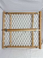 Front view of adjustable wooden safety gate showing white plastic mesh and sliding bar