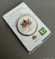 Front of coin in holder showing Canada 150 maple leaf design