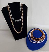 Four necklaces displayed; cloisonné on bust, clear faceted on bust, amber and pink coils on blue form