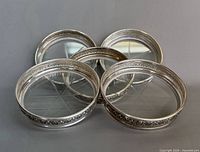 Five sterling-rimmed crystal coasters spread out