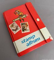 front cover of red stamp album with cartoon space figure and two sample stamps