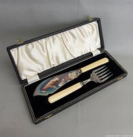 Open case showing knife and fork with cream handles inside white satin and black velvet lining