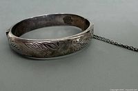 Full view of etched sterling bangle showing floral pattern and safety chain