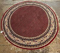 Full view of round red Persian design rug showing overall pattern and fringe