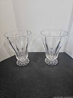 Two matching clear crystal vases on black surface