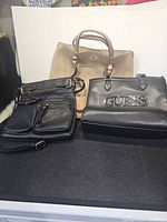 All three handbags side by side: black Guess logo bag, black crossbody, tan tote
