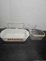 Group shot of three loaf pans: two clear Pyrex and one white Fire-King with fruit motif