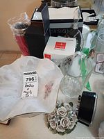 Overview of lot showing porcelain bowl, floral figurine, hexagonal pitcher, clock, boxed glassware