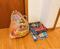Bag with colorful plastic interlocking blocks and two board game boxes on floor
