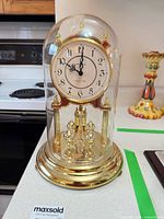 Full view of Howard Miller anniversary clock under glass dome showing base, columns and four-ball pendulum