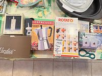 Group shot showing boxed Rotato peeler, espresso maker, paper towel holder, bottle opener, jar opener and boxed mugs