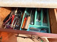 Drawer with flatware in turquoise tray and assorted utensils at left