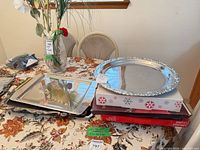 Stack including round silver tray atop boxed cake plate and rectangular trays on floral cloth