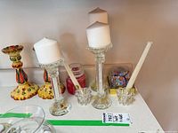 Group view showing crystal pillar holders with candles, ceramic candlesticks, small glass taper holders, jar candles, and boxed paperweight