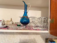 Shelf view showing blue ewer, wine goblets, teacups, shot glasses, swan figurine and jar
