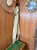 Full view of folded beige patio umbrella leaning against wood panel wall