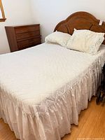 Full view of assembled queen bed showing wood headboard, bedding, dresser partially visible