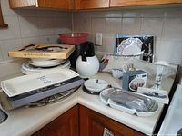 Assorted tableware and decor items on countertop including boxed platter, tea kettle, plates, boxed candle holders, swan figurine