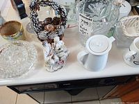 Overview of glassware, porcelain teapot, figurines, and pine-cone basket on countertop