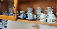 Cabinet shelf with blue geometric teapot and sugar bowl, six floral cups and saucers, floral creamer and sugar bowl