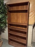 Front view of tall brown bookcase showing seven shelves and panel back