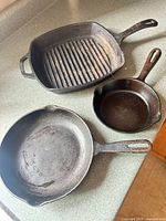 Three cast iron pans: square grill pan, medium and small skillets