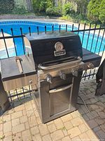 Front view of closed Cuisinart grill showing logo, control panel, side shelves and pool backdrop