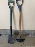 Both shovels standing side by side against wall