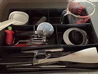 Group of utensils in drawer organizer including measuring cups, pizza cutter, slicer, corkscrew, tongs, scoop, spatula