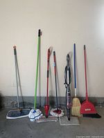 Group shot of seven floor cleaning tools standing against wall