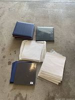 Top view of five scrapbooks, stack of paper, and page protectors on concrete floor