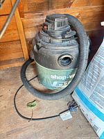 Full view of Shop-Vac canister vacuum with hose in shed