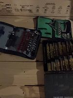 Three tool cases open showing drill bits, socket/bit set, hex keys
